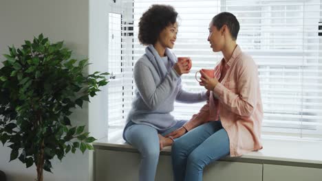 pareja de lesbianas tomando café sentada en el alféizar de la ventana