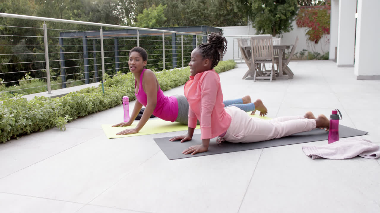 feliz hija afroamericana y madre practicando yoga en el jardín, cámara lenta