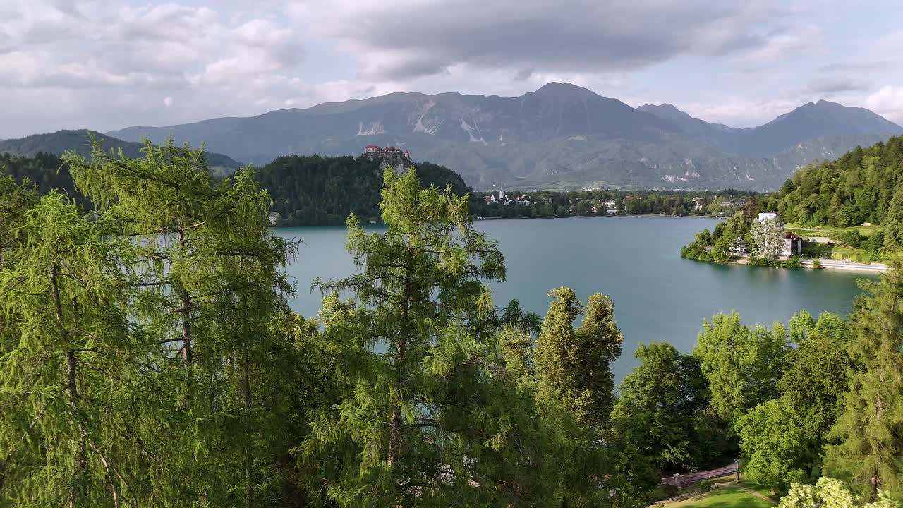 Lago e castello di Bled, volo orizzontale con drone oltre gli alberi, giornata estiva nuvolosa