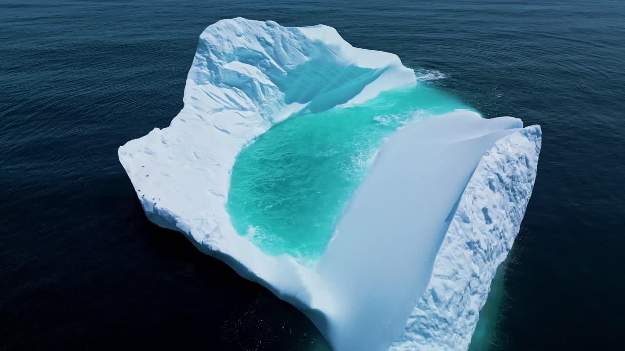 Aerial footage of a large iceberg off Flatrock, Newfoundland, featuring vivid turquoise meltwater in calm Atlantic waters.