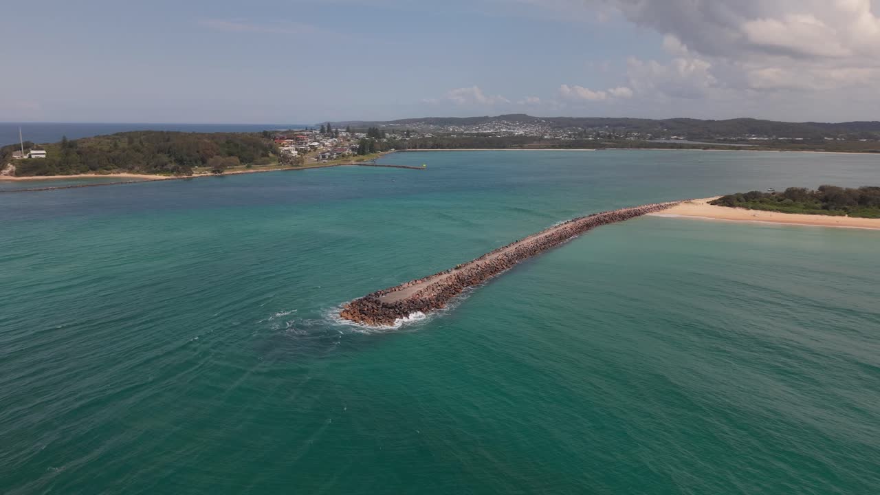Ocean breakwall from above, surrounded by white foam and deep blue ocean, NSW Australia