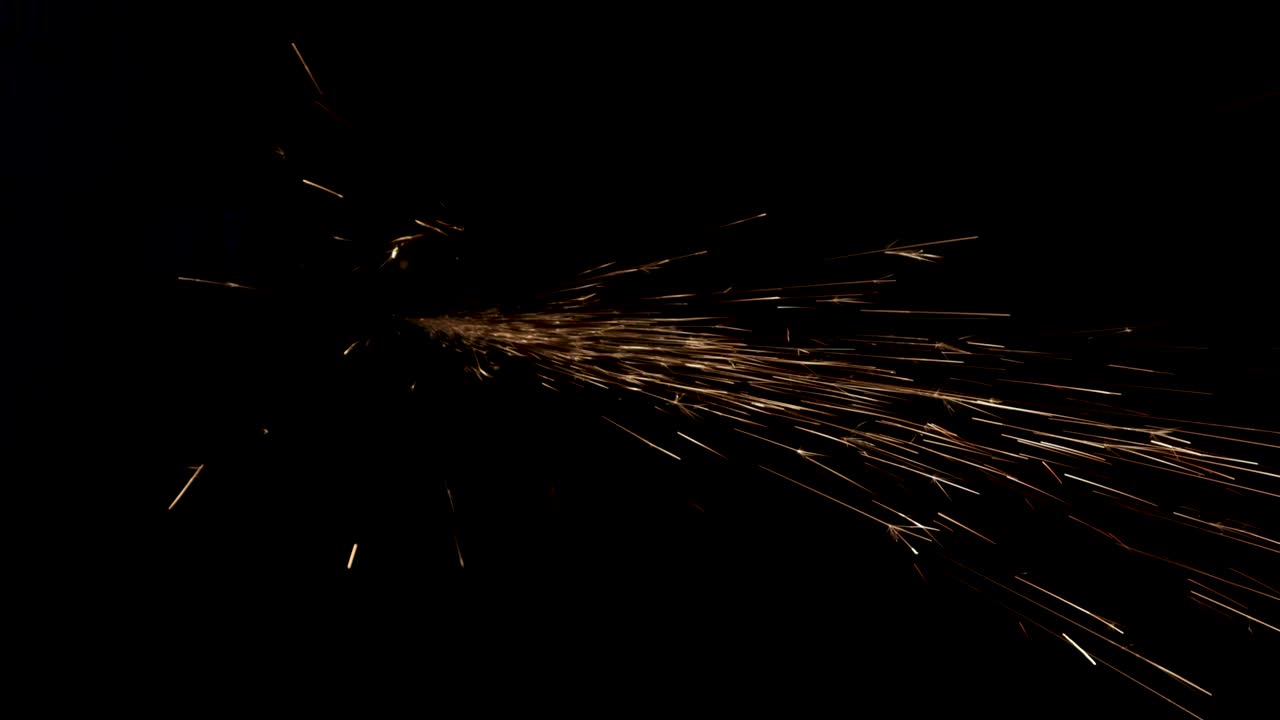 el hombre trabaja la sierra circular sobre el acero. las chispas vuelan desde el metal caliente sobre un fondo negro.