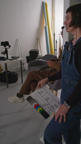 video vertical de asistente y directora frustrada con clapperboard mientras los actores filman una película o video en el estudio con el equipo de filmación y el director filmado en tiempo real