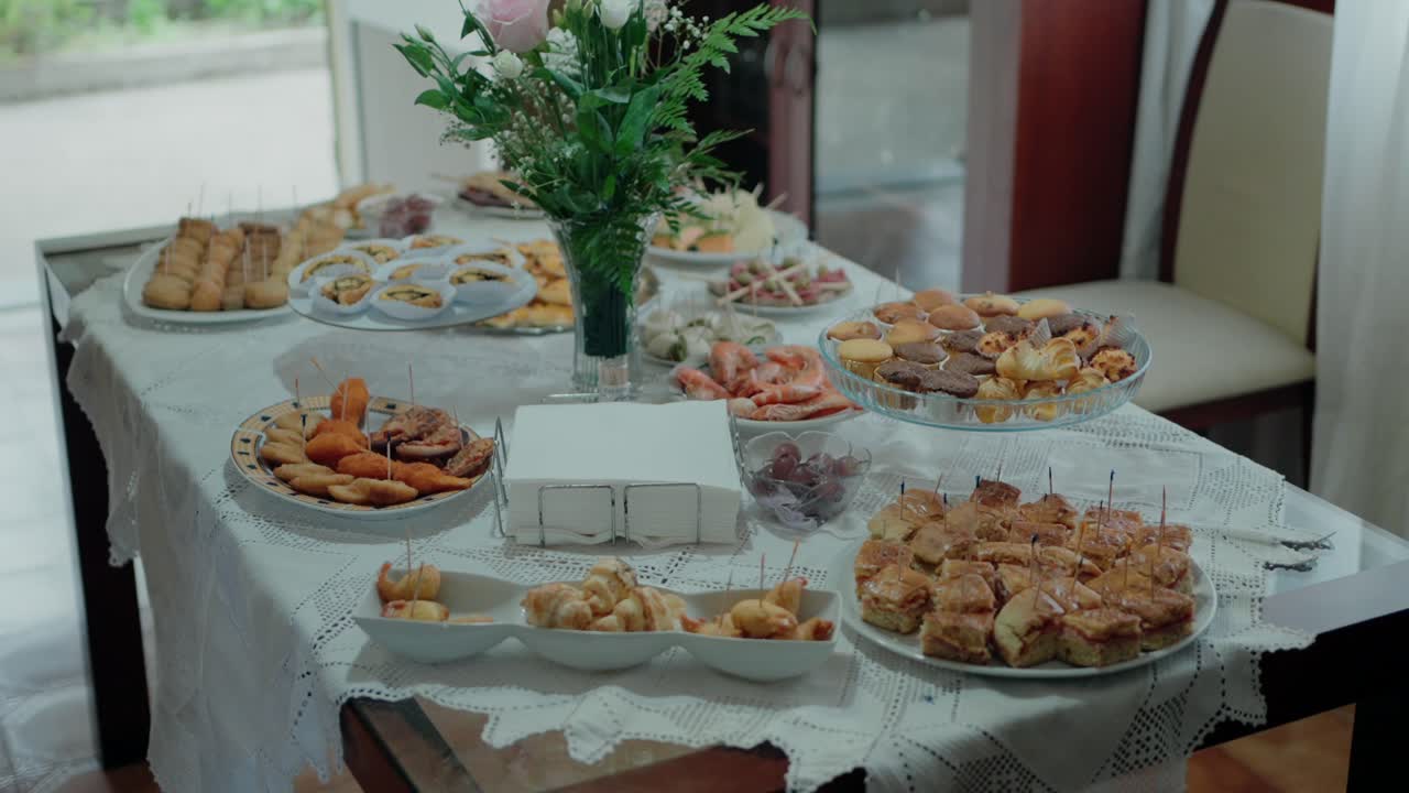 table set with various appetizers and finger foods, alongside a floral arrangement, in an indoor setting