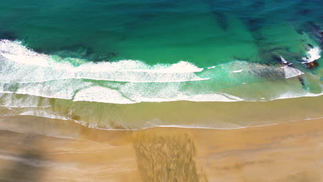 aerial top down of waves crashing in to unpolluted natural sandy golden beach in new zealand, dreamy paradise stunning holiday location