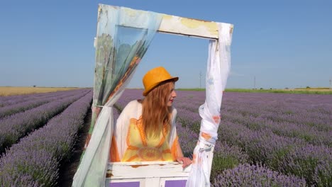 Panoramic-shot-from-young-woman-leaning-against-decorative-door-in-lavender-field-to-wooden-pole-with-decorative-signs