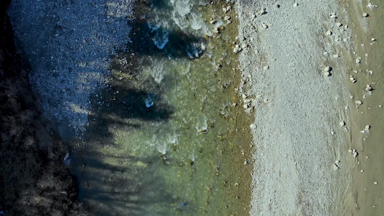 River water streaming through pebbles splashing on cliffs and foaming, water falling from mountains, aerial view following water