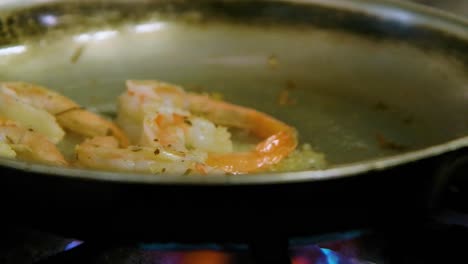 chef drizzles oil along pan of shrimp on gas stove, flame bursts into air around steam