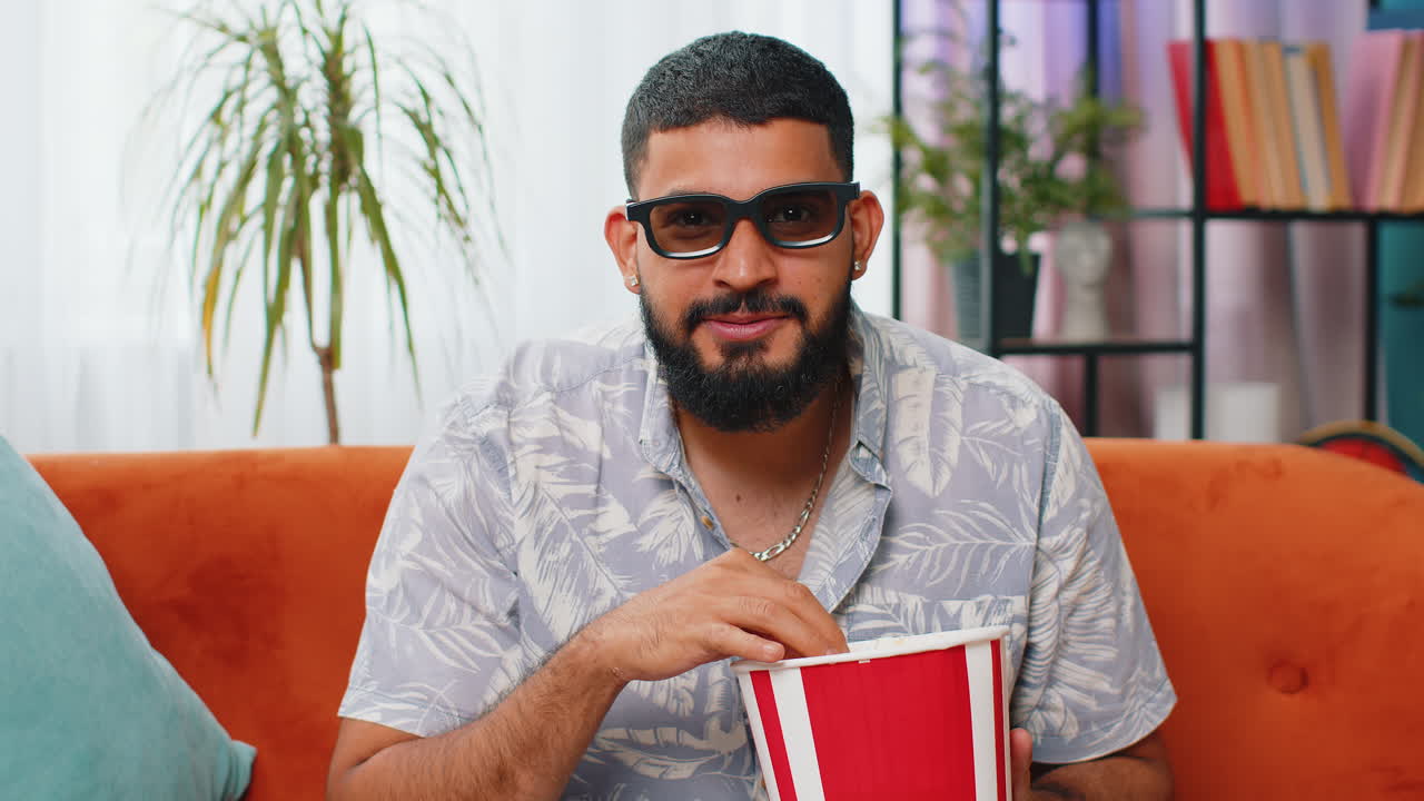 Arabian man sit on couch eating popcorn watching interesting tv serial sport game online at home