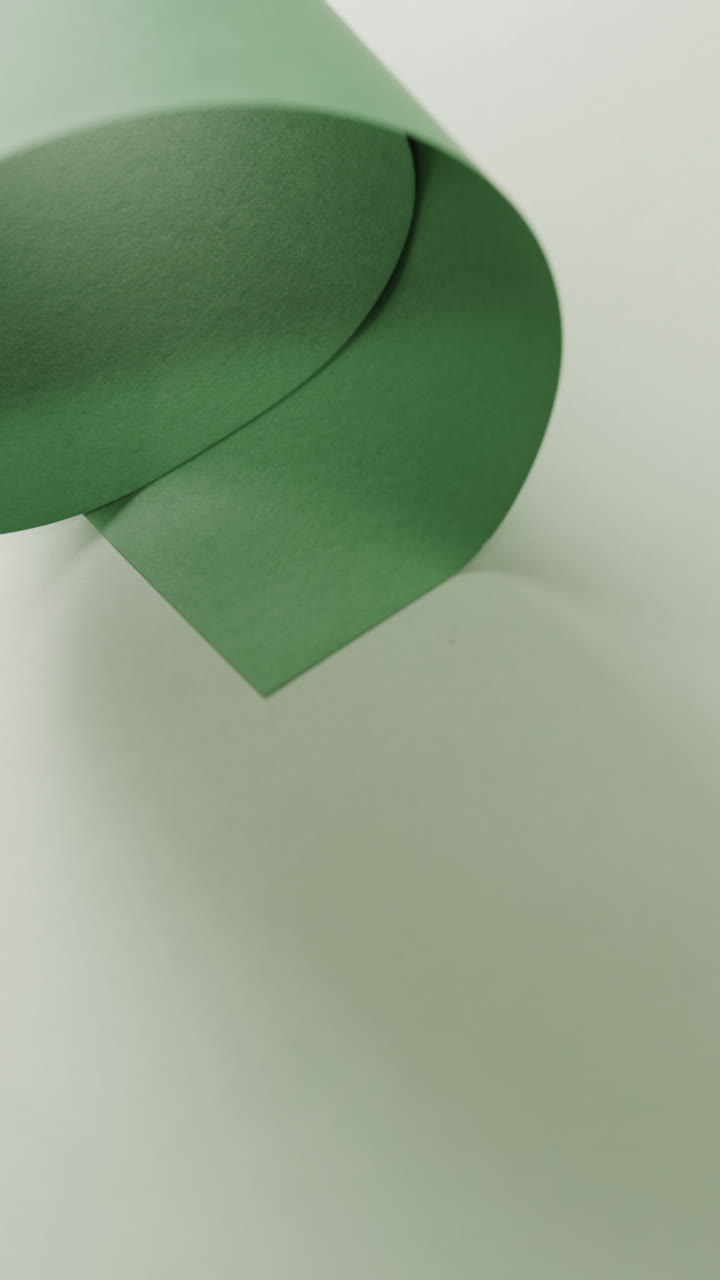 Vertical video of close up of green rolled paper on pale green background with copy space