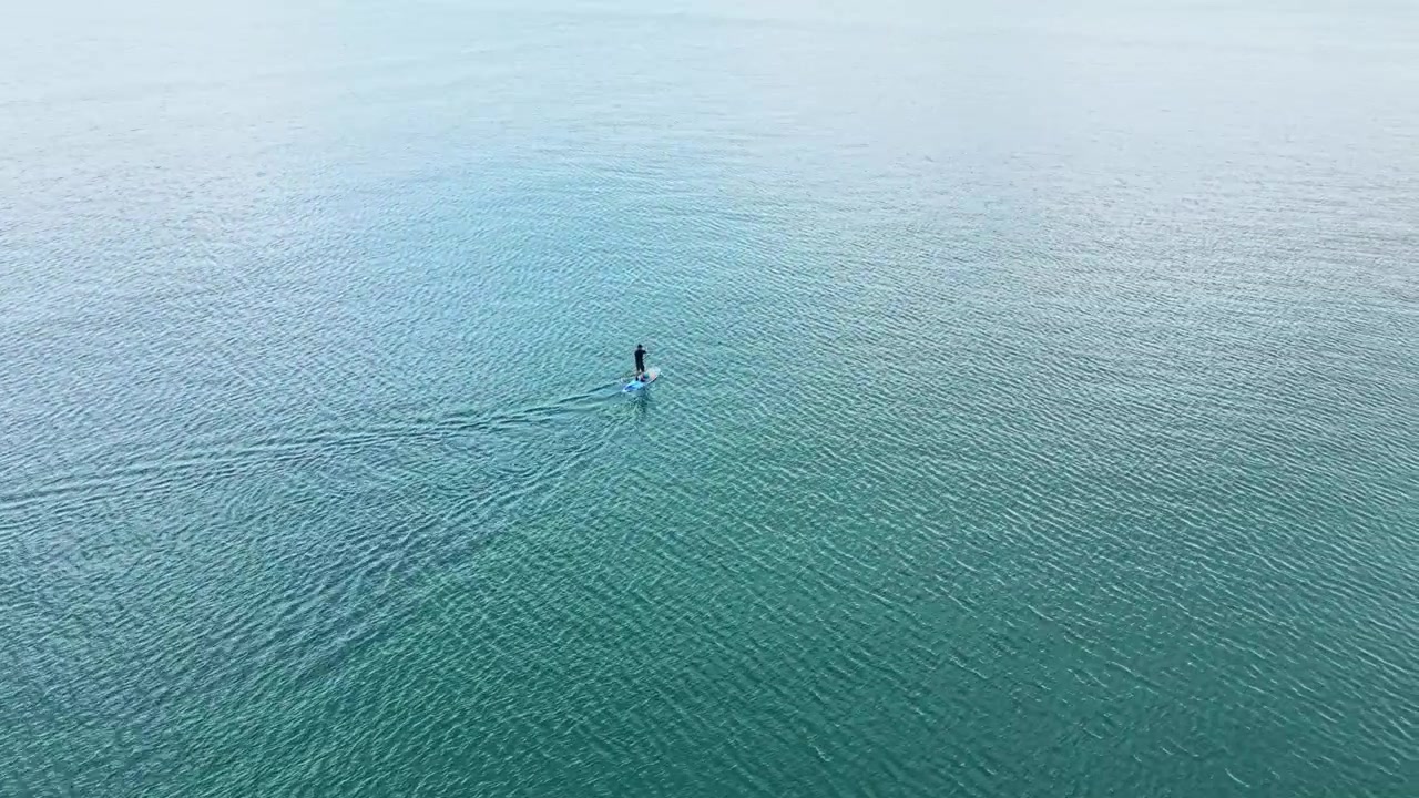 Un surfeur sur un paddleboard sur des eaux calmes tôt le matin dans une zone côtière