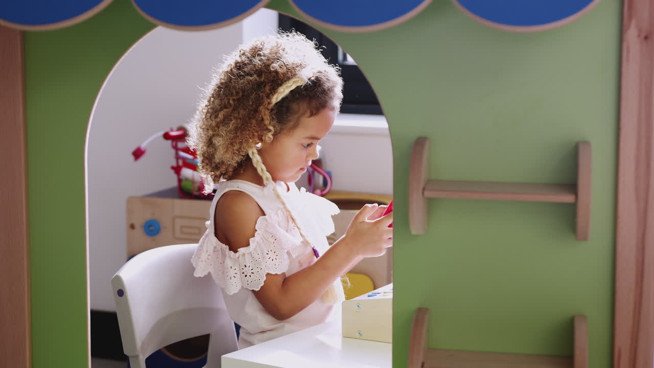 Young mixed race schoolgirl playing shop in a playhouse at an infant school, backlit
