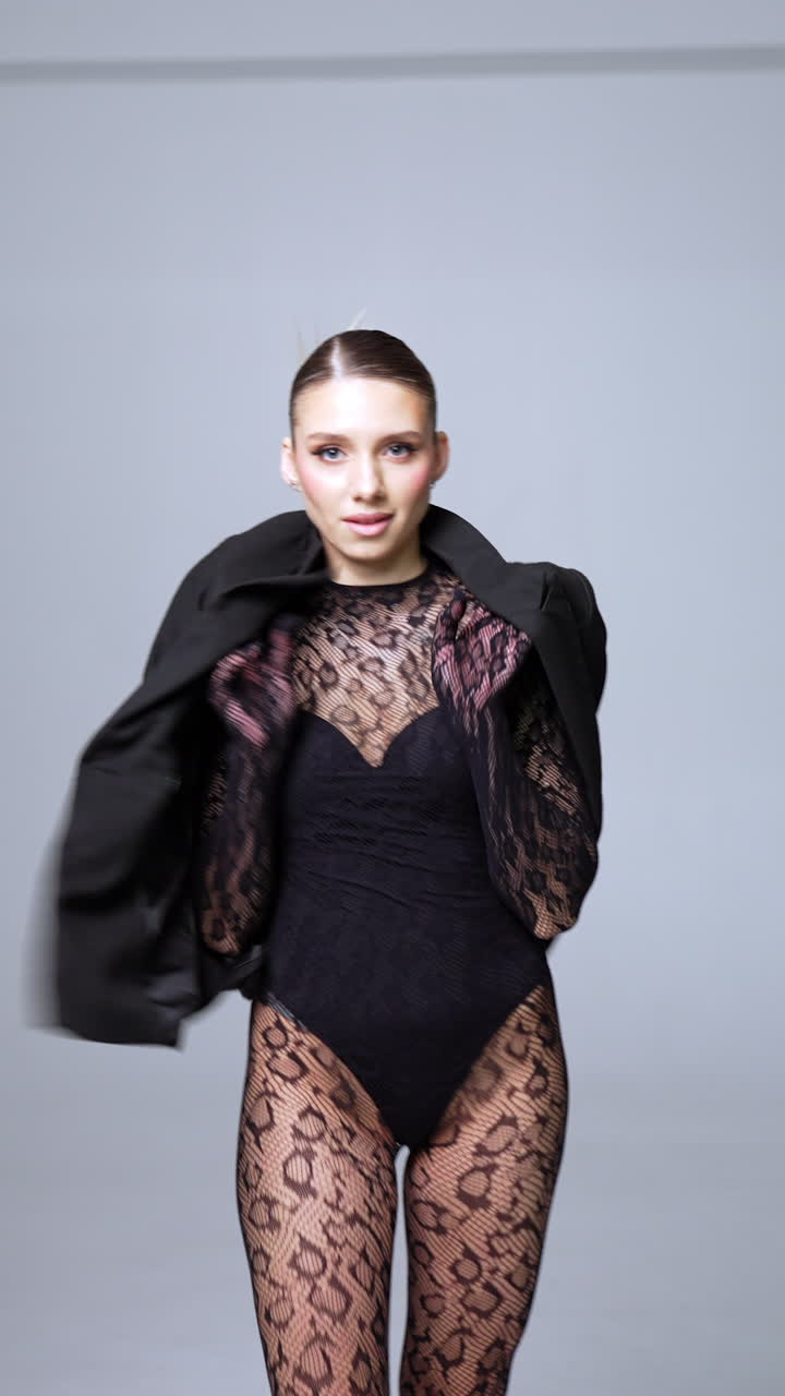 Gorgeous Caucasian lady wearing sexy lace outfit and high heels. Model puts on black jacket. Studio footage. Vertical video.
