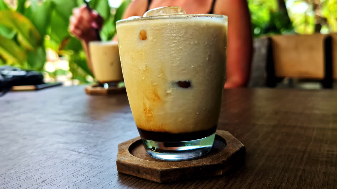 Iced latte with milk foam on wooden table at tropical cafe