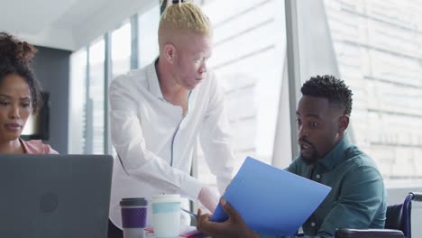 Diverse-business-people-discussing-with-disabled-colleague-and-documents-in-creative-office