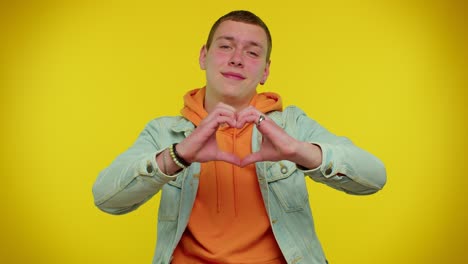 Smiling-teen-man-makes-heart-gesture-demonstrates-love-sign-expresses-good-feelings-and-sympathy