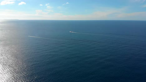 two motor boats moving from right to left with the horizon in the background and the sun shine coming from the left