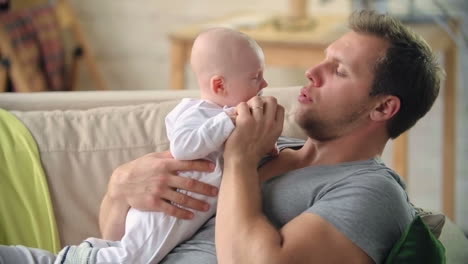 Father-Lying-On-The-Sofa-Holding-His-Baby-And-Showing-Him-Affection