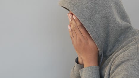 person in a hoodie with hands over face