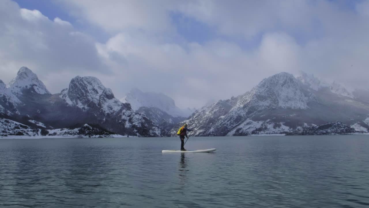 해안의 물과 산 사이에 패들 보드를 탄 남자