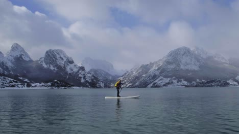 man on paddle board between water and mountains on coast