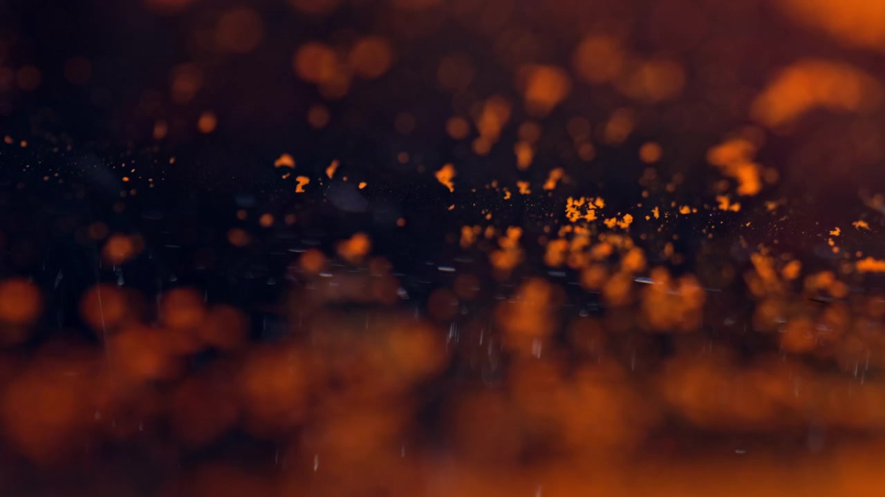 Orange chemical pigment spreads and scatters across a green liquid surface in a warm, shallow-focus macro shot.