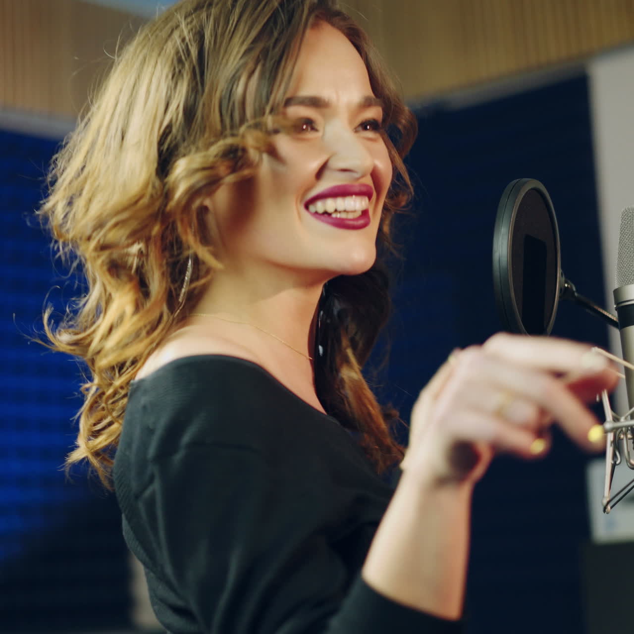 Wonderful woman dancing and singing merrily in front of a professional mic on a background of recording studio. Happy musician standing at microphone and performing new music