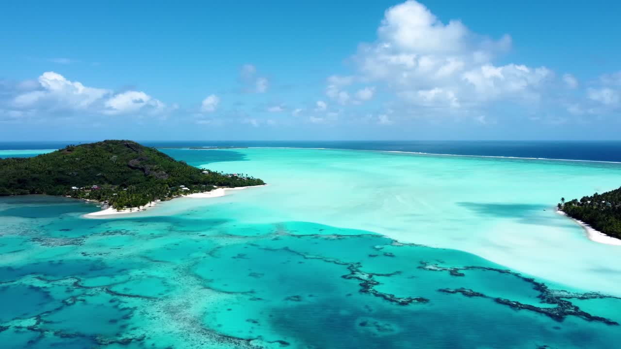 Drone view of a small green pacific tropical island with a lagoon, coral reef, white sand beach and blue shallow water on a sunny day in Maupiti, French Polynesia.