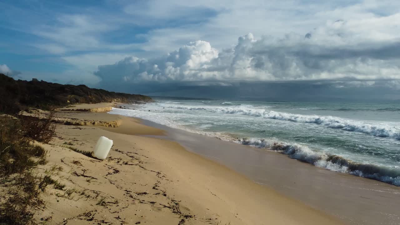 Contenitore di plastica singolo su una spiaggia remota in Spagna con nuvole minacciose sopra