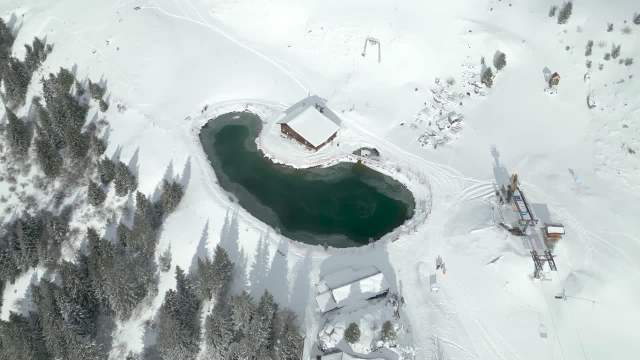 Güneşli bir günde İsviçre'deki Engelberg Brunni bahnen'de telesiyej yanında kısmen donmuş göl üzerinde havadan drone çekimi