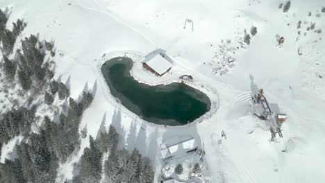 Avión-Teledirigido-De-Arriba-Hacia-Abajo-Sobre-Un-Lago-Parcialmente-Congelado-Junto-Al-Telesilla-En-Engelberg-Brunni-Bahnen,-Suiza,-En-Un-Día-Soleado