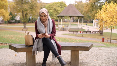 british muslim woman texting on mobile phone in park