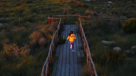 adorable young girl running along a boardwalk to go to the beach in winter at sunset