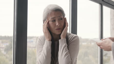 sick woman sitting by the window having a severe headache while her husband giving her an ice pack and trying to comfort her