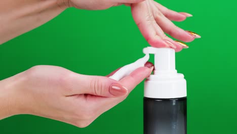 female hands pushing dispenser and using liquid soap on green background. prevention of viruses, safety protection. antibacterial foaming sanitizer close-up