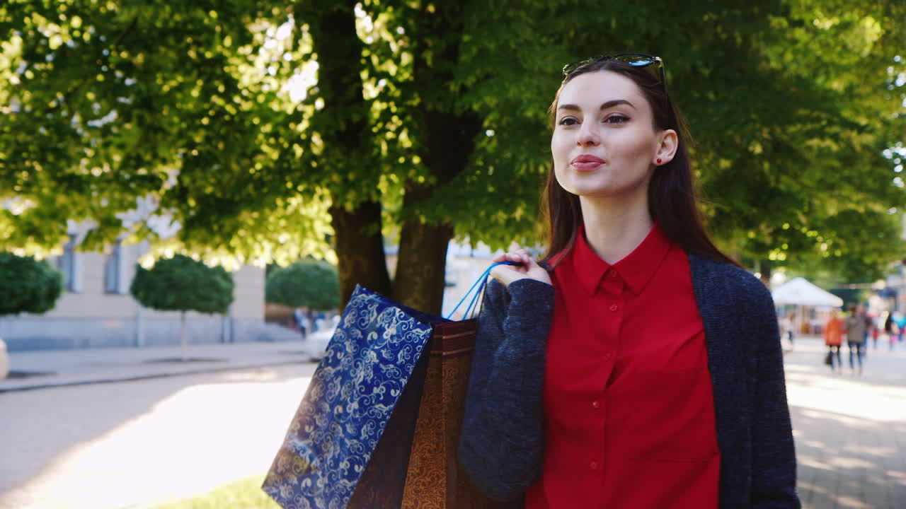 쇼핑백을 든 빨간 드레스를 입은 세련된 여성 dyal은 태양이 아름답게 빛나는 도시를 산책합니다.