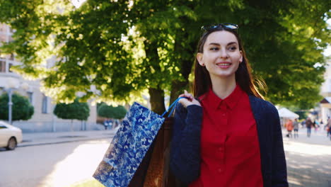 mujer elegante en un vestido rojo con bolsas de compras dyal camina por la ciudad el sol brilla hermoso