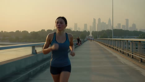 woman running on a bridge with city skyline at sunrise or sunset