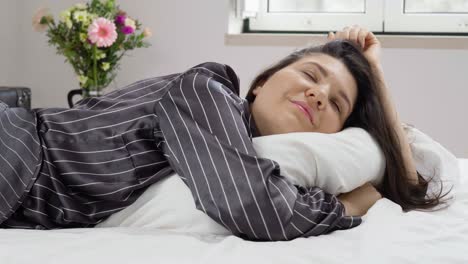 Young-woman-in-black-pajamas-lying-on-the-bed-hugging-pillow-and-dreaming