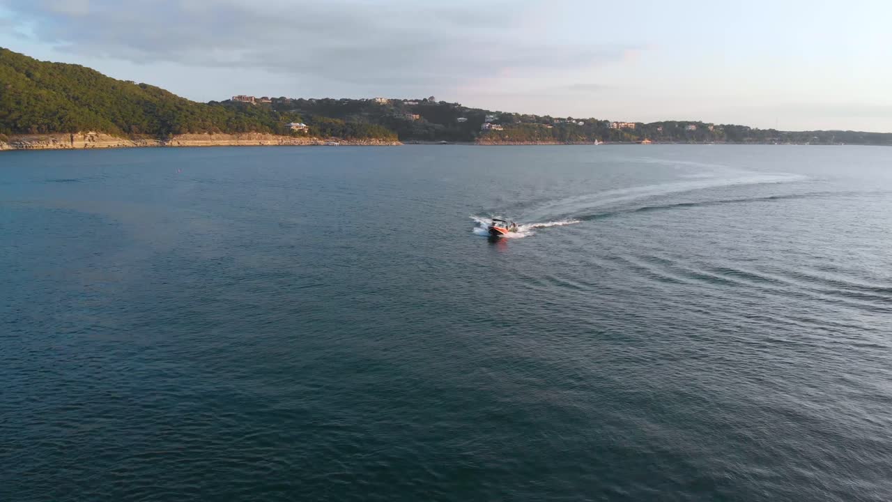toma panorámica hacia atrás de un bote tirando de un tubo en el lago travis que revela los acantilados en el fondo