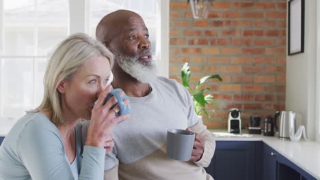 Una-Pareja-De-Ancianos-De-Raza-Mixta-Tomando-Café-Juntos-En-La-Cocina-De-Casa