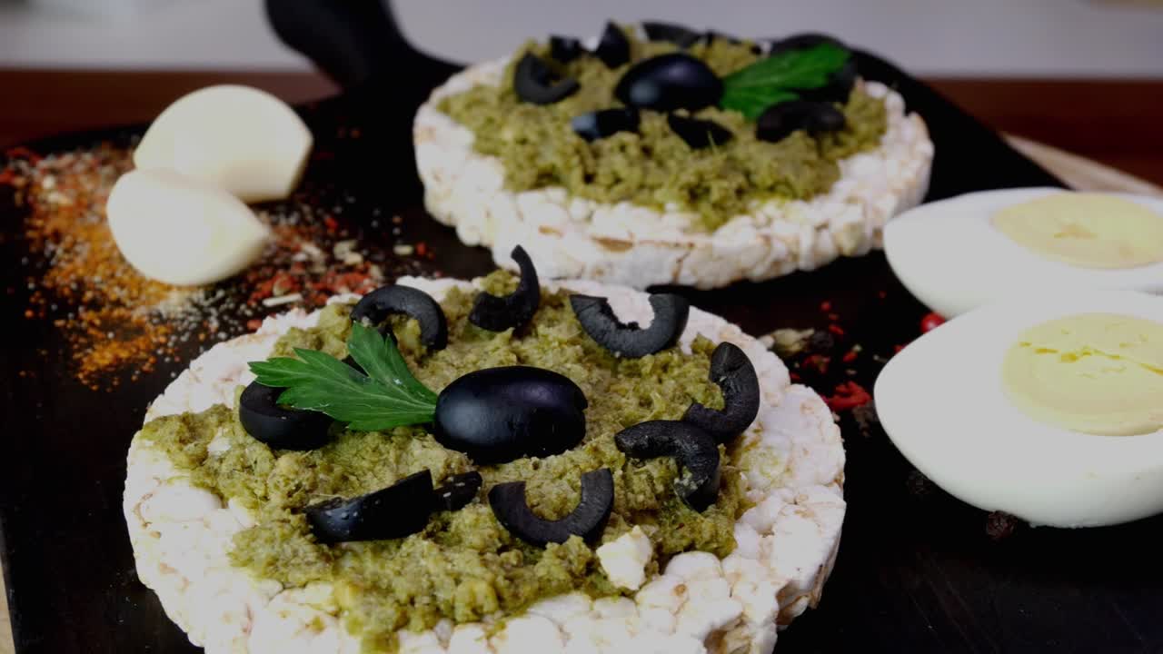 las tostadas de pastel de arroz con salsa de pesto verde y huevos hervidos giran lentamente en la tabla de cortar.