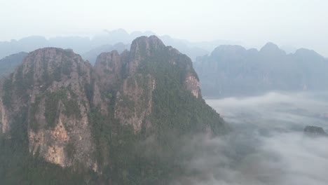 drone shot flying over cliffs and misty valley in vang vieng, the adventure capital of laos