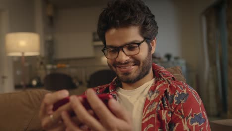 joven indio sentado en el sofá viendo una película en ott en el teléfono móvil en casa