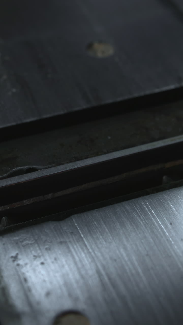 Metalindsats til bord med central rille og bolthuller, subtile refleksioner, savsmuldsflager og slidt arbejdsplade.