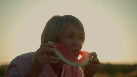 woman enjoying a refreshing bite of watermelon slice with love-shaped cutout under bright summer sky, sunlight creates a romantic silhouette while vibrant red fruit