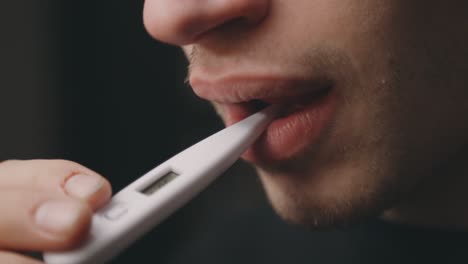 un hombre caucásico enfermo se pone un termómetro médico en la boca para comprobar la temperatura corporal