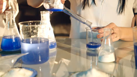 doctor is pouring chemicals from the test tube into the glass jar on the table on the background of glass tanks in the laboratory