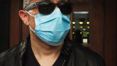 man walks outside, wearing covid-19 surgical mask and sunglasses