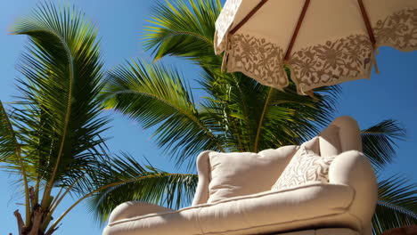 a comfortable outdoor armchair under a palm tree and umbrella